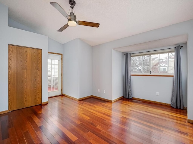 unfurnished bedroom featuring ceiling fan, visible vents, wood finished floors, baseboards, and lofted ceiling