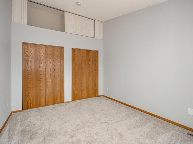 unfurnished bedroom featuring multiple closets, baseboards, carpet flooring, and visible vents