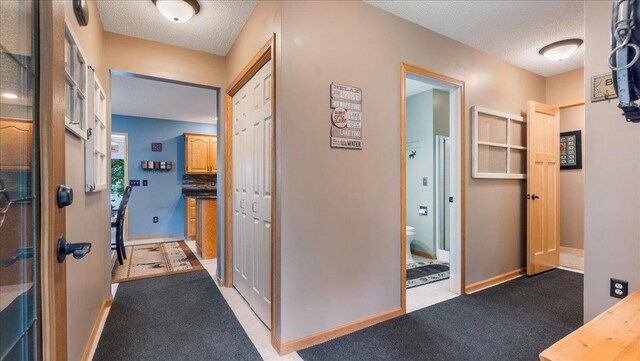 hall featuring baseboards, a textured ceiling, and light colored carpet