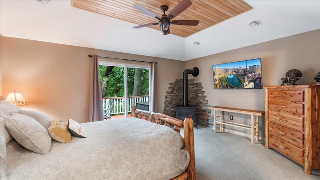 carpeted bedroom with access to exterior, vaulted ceiling, ceiling fan, wood ceiling, and a wood stove