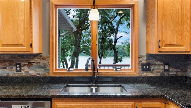 kitchen with dark countertops, dishwasher, a sink, decorative light fixtures, and tasteful backsplash