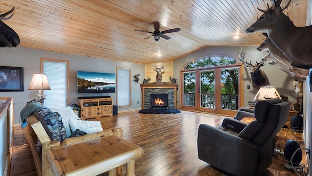 living area featuring vaulted ceiling, wood finished floors, ceiling fan, wooden ceiling, and a stone fireplace