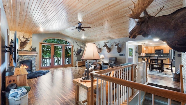 interior space with vaulted ceiling, a ceiling fan, wood finished floors, a stone fireplace, and wooden ceiling