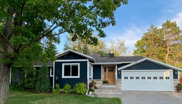 ranch-style home featuring an attached garage, concrete driveway, a chimney, a front lawn, and stone siding