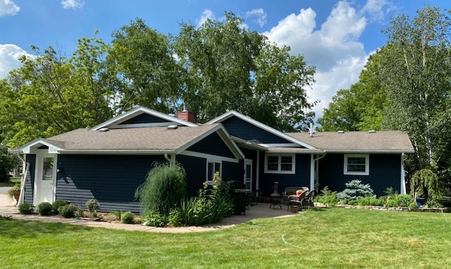back of house featuring a chimney, a lawn, a patio area, and a shingled roof