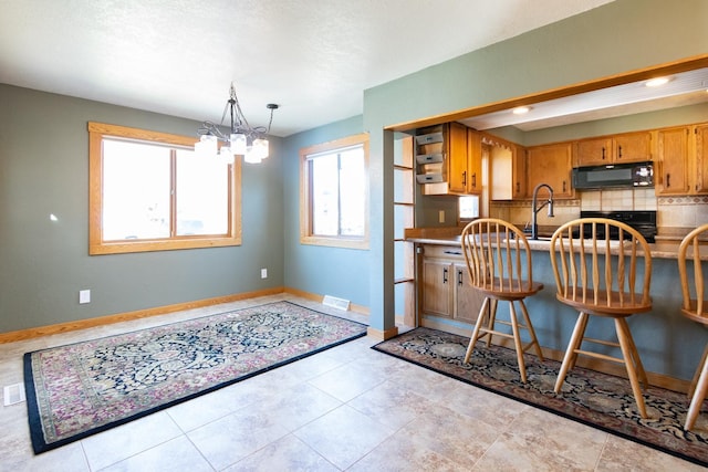 kitchen featuring black microwave, decorative backsplash, a chandelier, range, and brown cabinetry