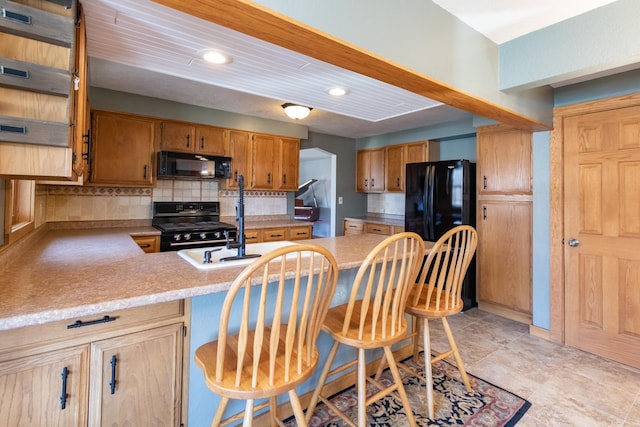 kitchen with black appliances, backsplash, a peninsula, light countertops, and a breakfast bar area