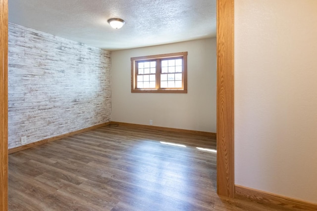 empty room featuring a textured ceiling, baseboards, and wood finished floors