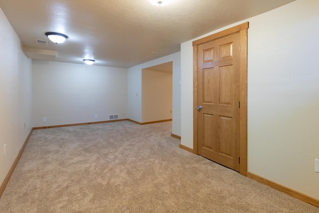 spare room with light carpet, baseboards, and a textured ceiling