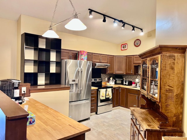 kitchen with appliances with stainless steel finishes, under cabinet range hood, track lighting, backsplash, and hanging light fixtures