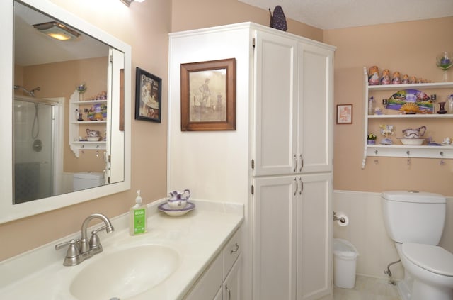 full bath featuring toilet, a stall shower, vanity, and a wainscoted wall