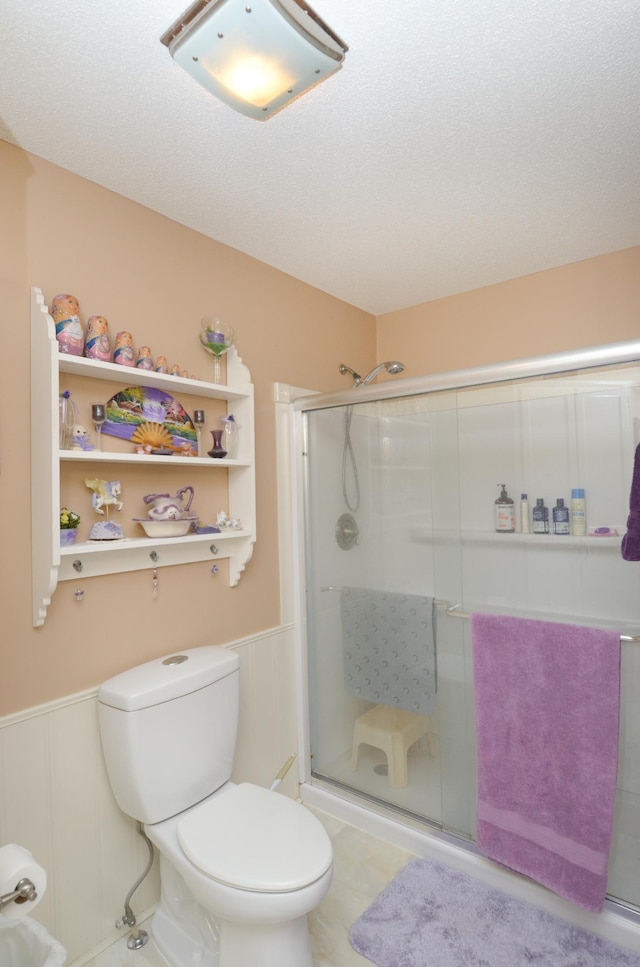 full bath with a stall shower, a wainscoted wall, toilet, and a decorative wall