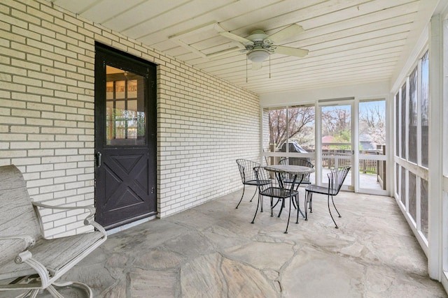 sunroom with a healthy amount of sunlight, ceiling fan, and brick wall
