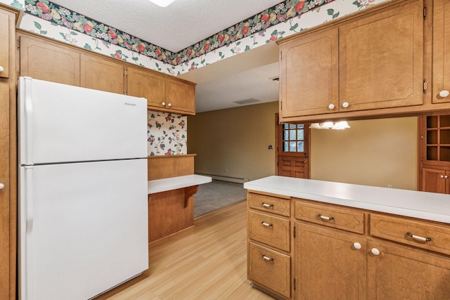 kitchen with brown cabinets, light countertops, freestanding refrigerator, a baseboard heating unit, and light wood-style flooring