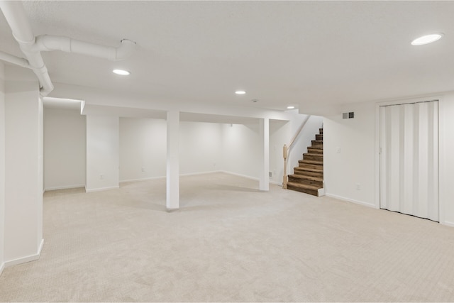 finished basement with visible vents, baseboards, recessed lighting, stairway, and light carpet