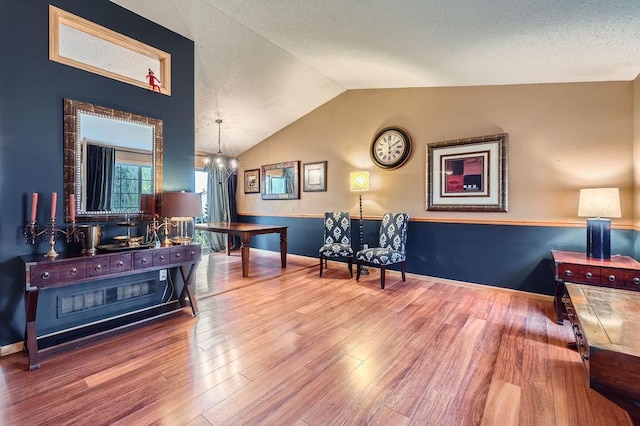 sitting room with wood finished floors, a textured ceiling, lofted ceiling, and an inviting chandelier