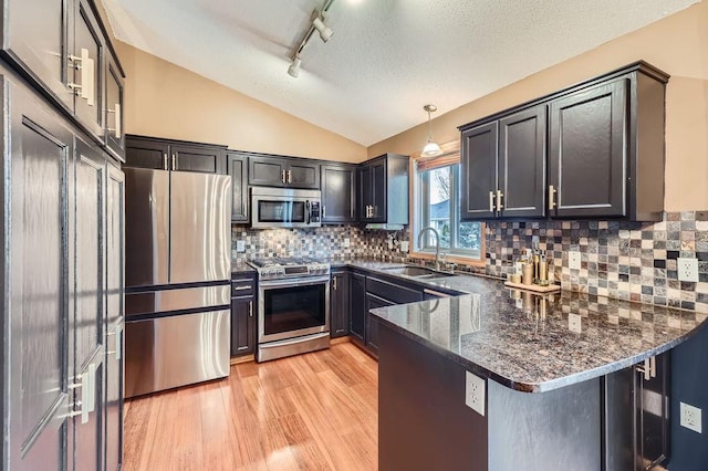 kitchen featuring a sink, stainless steel appliances, light wood finished floors, a peninsula, and lofted ceiling