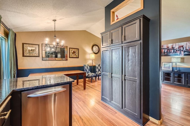 kitchen with dark stone counters, stainless steel dishwasher, an inviting chandelier, light wood finished floors, and lofted ceiling