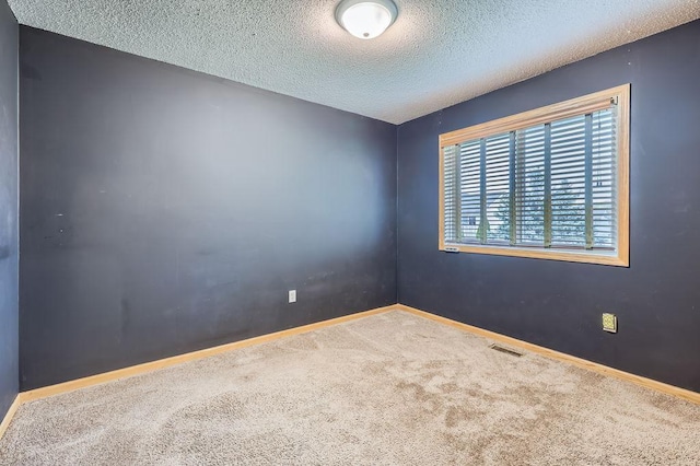 empty room with a textured ceiling, carpet, visible vents, and baseboards