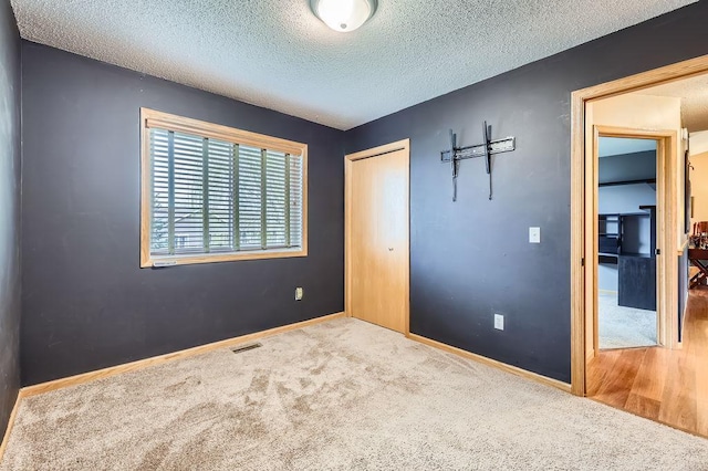 unfurnished bedroom with a textured ceiling, carpet, visible vents, and a closet