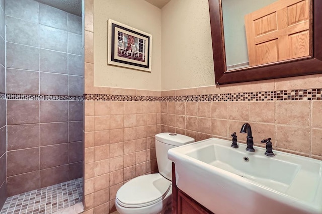 bathroom featuring a tile shower, tile walls, toilet, and vanity