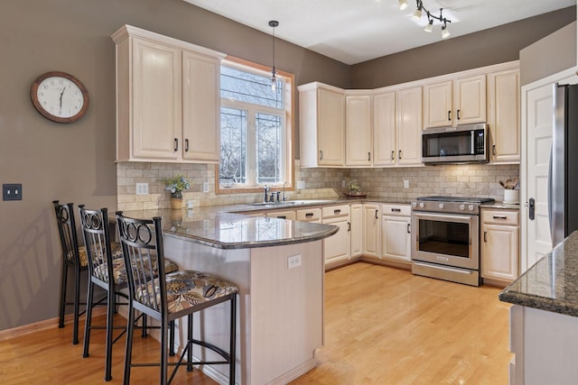 kitchen featuring light wood finished floors, a sink, decorative backsplash, a peninsula, and appliances with stainless steel finishes