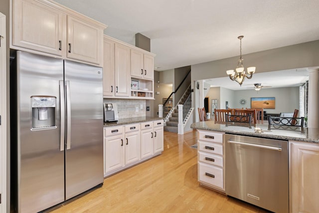 kitchen featuring light wood finished floors, tasteful backsplash, pendant lighting, stone countertops, and appliances with stainless steel finishes