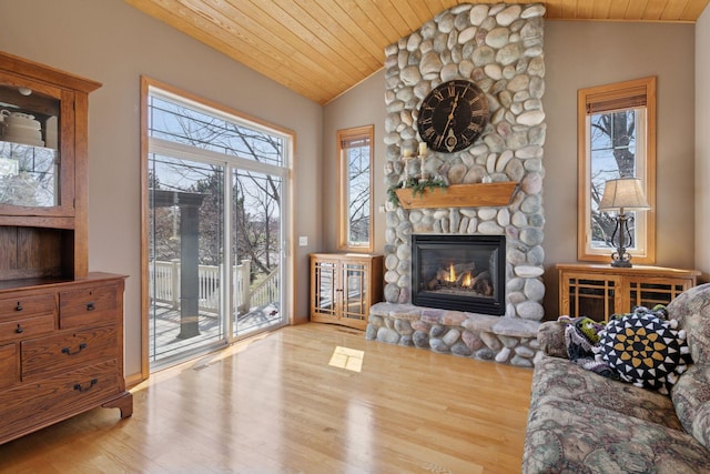 living room with wood ceiling, lofted ceiling, wood finished floors, and a stone fireplace