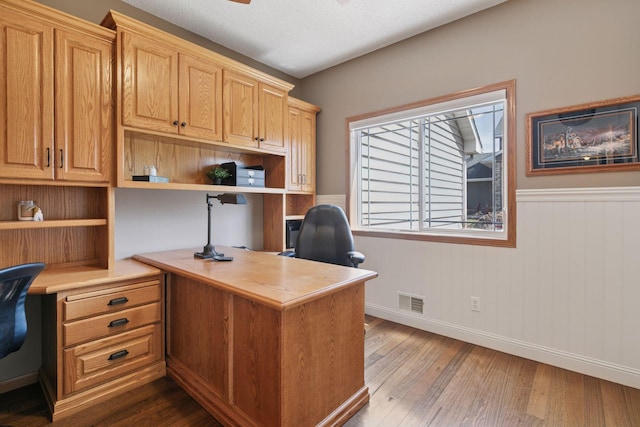 office space featuring dark wood-style flooring, wainscoting, baseboards, visible vents, and built in study area