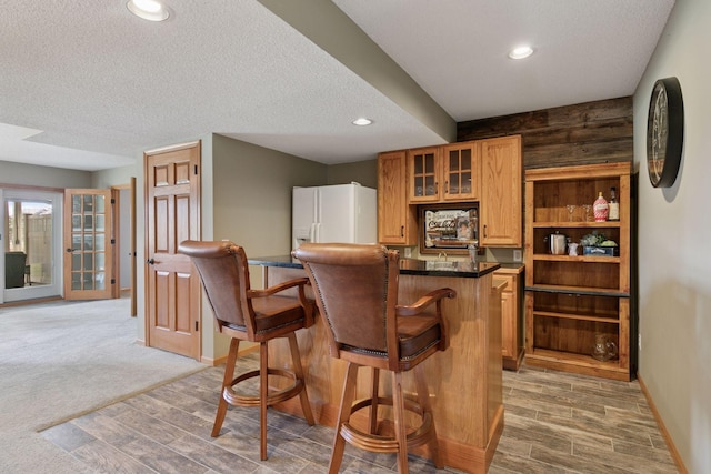 bar with light wood-type flooring, baseboards, white fridge with ice dispenser, and a textured ceiling