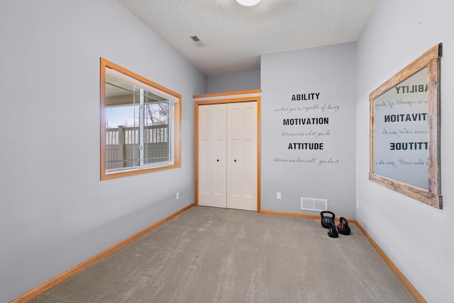 unfurnished bedroom featuring a textured ceiling, a closet, baseboards, carpet flooring, and visible vents