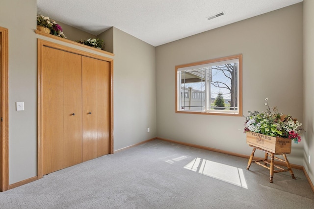 unfurnished bedroom featuring baseboards, visible vents, a textured ceiling, and light colored carpet