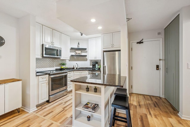 401 1st St Unit 308, Minneapolis, MN 55401 - kitchen with appliances with stainless steel finishes, open shelves, light wood finished floors, white cabinetry, and a kitchen bar