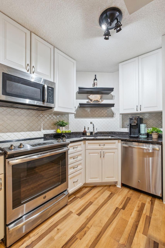 401 1st St Unit 308, Minneapolis, MN 55401 - kitchen with appliances with stainless steel finishes, open shelves, dark countertops, light wood-style flooring, and a textured ceiling