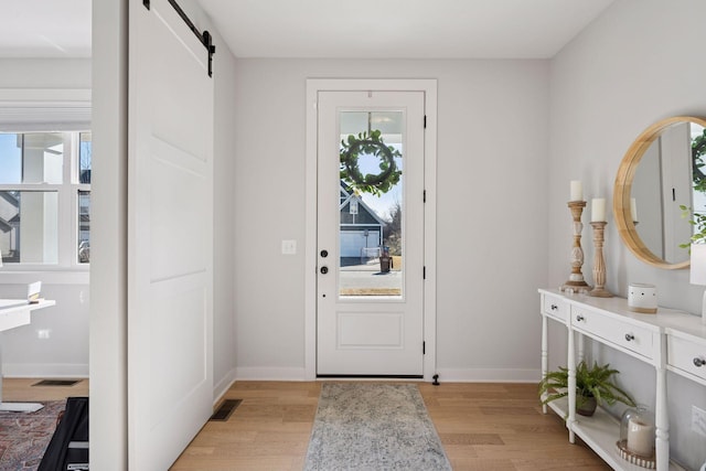 entryway with light wood-style flooring, baseboards, visible vents, and a barn door