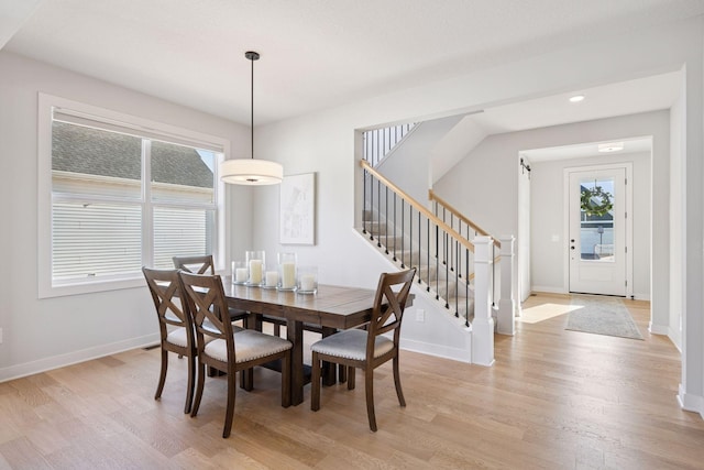 dining room featuring light wood finished floors, baseboards, and stairs