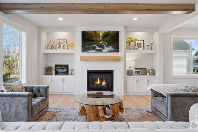 living room featuring beam ceiling, built in shelves, light wood-style floors, and a fireplace