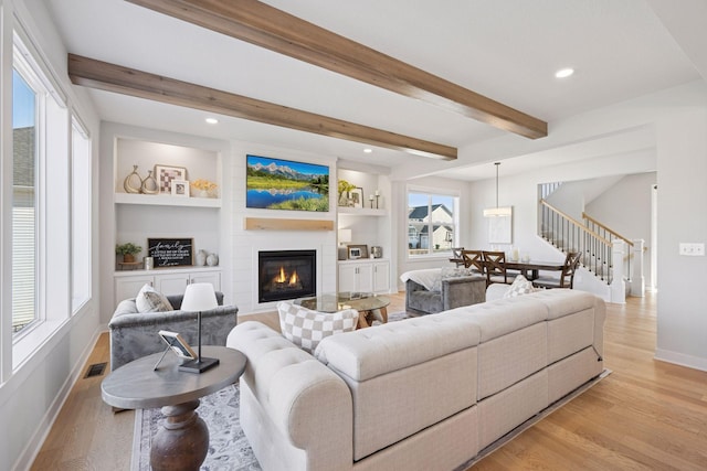 living area with a fireplace, stairway, light wood-style flooring, visible vents, and beamed ceiling