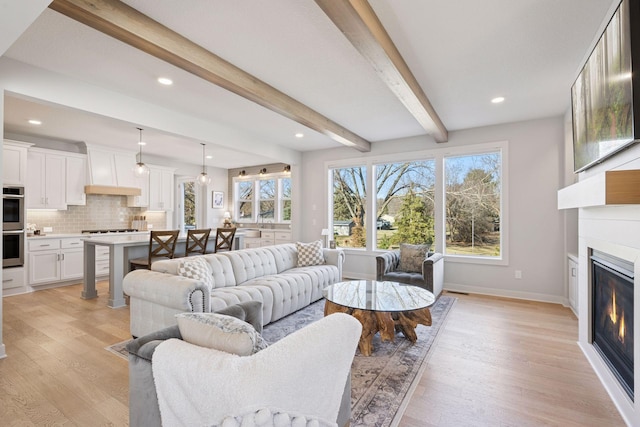 living room featuring a fireplace, light wood-style flooring, recessed lighting, baseboards, and beam ceiling