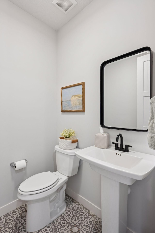 half bath featuring a sink, visible vents, toilet, and baseboards