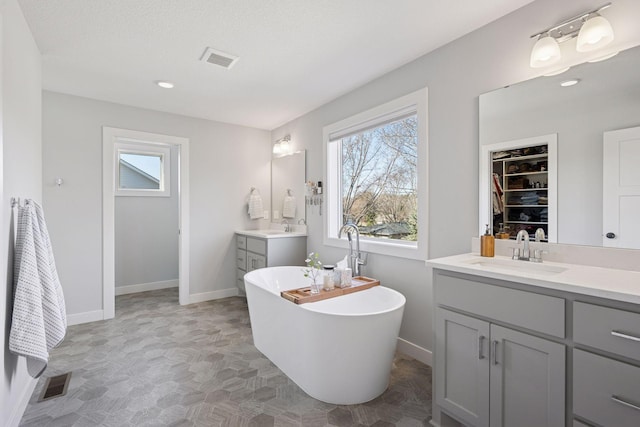 full bath with baseboards, two vanities, a sink, and visible vents