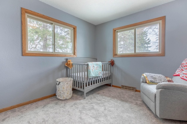 carpeted bedroom featuring multiple windows, a nursery area, and baseboards