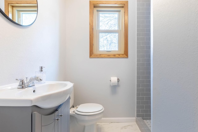 full bathroom featuring a tile shower, toilet, vanity, marble finish floors, and baseboards