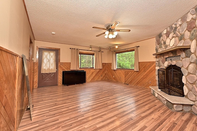 unfurnished living room with a wainscoted wall, light wood-style floors, wood walls, a fireplace, and a ceiling fan