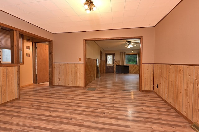 empty room featuring wooden walls, a wainscoted wall, light wood finished floors, and ceiling fan
