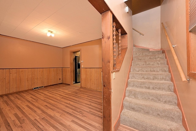 stairway with wood finished floors, a wainscoted wall, and wooden walls