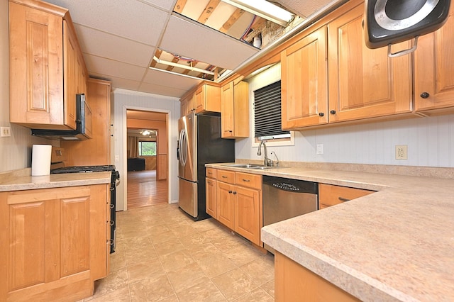 kitchen featuring appliances with stainless steel finishes, a sink, light countertops, light brown cabinetry, and a drop ceiling