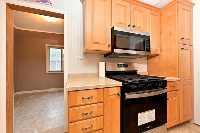kitchen with range with gas stovetop, stainless steel microwave, light countertops, light brown cabinetry, and baseboards