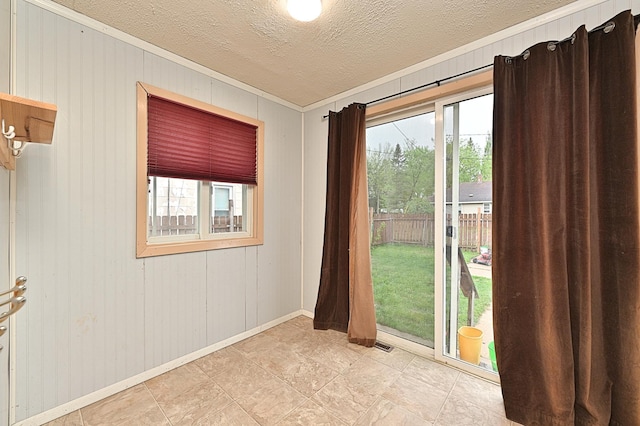 unfurnished room featuring ornamental molding, healthy amount of natural light, a textured ceiling, wood walls, and baseboards