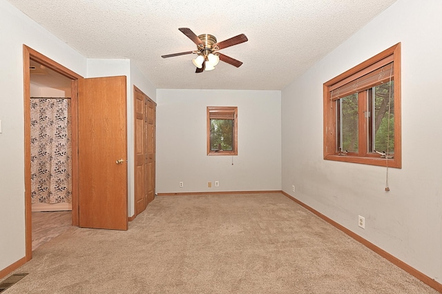 unfurnished bedroom with light carpet, a textured ceiling, baseboards, and a ceiling fan